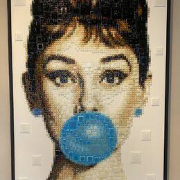 George Michael – GlassArt van Tessa van Thienen George Michael van glaskunstenares Tessa van Thienen is een krachtig en iconisch GlassArt-kunstwerk waarin muziek, stijl en emotie samenkomen. In haar herkenbare pop-art stijl weet Tessa de charismatische uitstraling, kwetsbaarheid en tijdloze klasse van George Michael treffend te vangen. Geïnspireerd door de muziek- en modewereld vertaalt zij zijn persoonlijkheid naar een gelaagd portret van duizenden zorgvuldig gesneden stukjes glas, samengesmolten tot een glamoureus en expressief geheel. Het spel van licht, kleur en diepte geeft het werk een levendige uitstraling die blijft veranderen afhankelijk van het perspectief. Dit bijzondere portret is een echte statement piece en perfect voor liefhebbers van moderne kunst, popcultuur en iconische muzieklegendes. Een eerbetoon aan een artiest die generaties blijft inspireren, uitgevoerd in de verfijnde en exclusieve glastechniek van Tessa van Thienen.